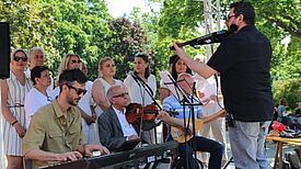 Eine Musikgruppe mit Chor, Keyboarder, Violinist und Gitarrist tritt auf einer Bühne im Freien vor Publikum beim Sommerfest im QM-Gebiet Brunnenstraße auf.