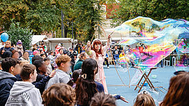 Junge Menschen staunen über riesige Seifenblasen einer Seifenblasenkünstlerin