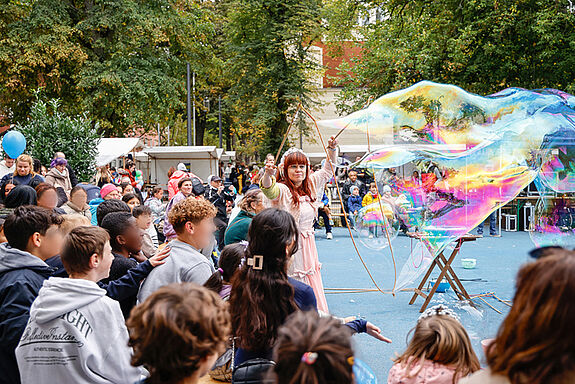 Junge Menschen staunen über riesige Seifenblasen einer Seifenblasenkünstlerin