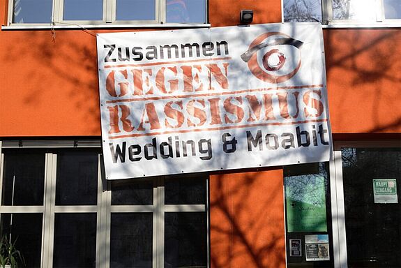 An einer Hauswand hängt ein Banner mit der Aufschrift „Zusammen gegen Rassismus Wedding & Moabit“.