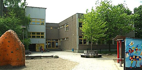 Der Schulhof der Grundschule am Amalienhof mit einem Spielplatz im Vordergrund und dem Schulgebäude im Hintergrund. 