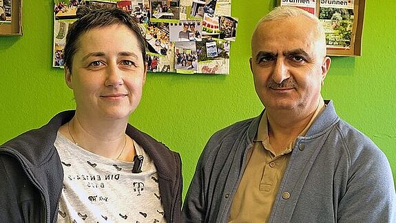 Zwei Personen stehen vor einer grünen Wand mit Fotos im Brunnenviertel.