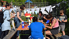 Mehrere Teilnehmende sitzen um einen Tisch und gestalten gemeinsam Wimpelketten. 