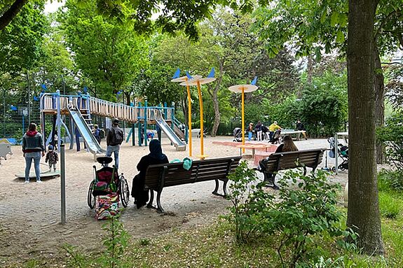 Kinder und Erwachsene nutzen bei sonnigem Wetter den Pumptrack und die Spielgeräte auf dem Spielplatz Silbersteinstraße im QM-Gebiet Glasower Straße.