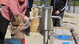 Jugendstadträtin Mirjam Blumenthal und der kleine Sohn von Baustadtrat Jochen Biedermann nehmen die Wasserpumpe in Betrieb. (Bild: Jens Sethmann)