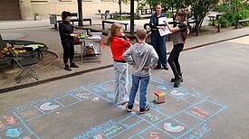 Kinder spielen auf dem Schulhof im QM-Gebiet Donaustraße-Nord ein Kreidespiel mit Würfel.