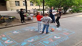 Kinder spielen auf dem Schulhof im QM-Gebiet Donaustraße-Nord ein Kreidespiel mit Würfel.