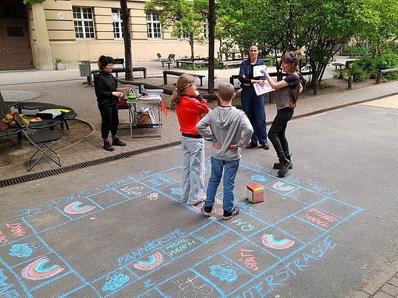 Kinder spielen auf dem Schulhof im QM-Gebiet Donaustraße-Nord ein Kreidespiel mit Würfel.