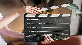 Eine Person hält eine Filmklappe vor sich.