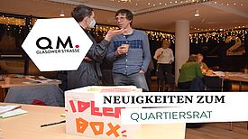 Zwei Personen sprechen miteinander. Vor ihnen steht auf einem Tisch eine Ideen-Box.