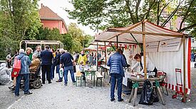 Menschen unterhalten sich zwischen Marktständen, an denen auch Speisen ausgegeben werden.