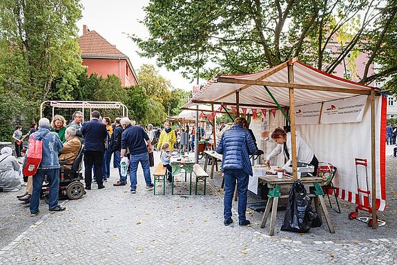 Menschen unterhalten sich zwischen Marktständen, an denen auch Speisen ausgegeben werden.