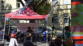 Unter einem roten Pavillon treten Musikerinnen und Musiker bei einem Nachbarschaftskonzert auf dem Kranoldplatz auf.