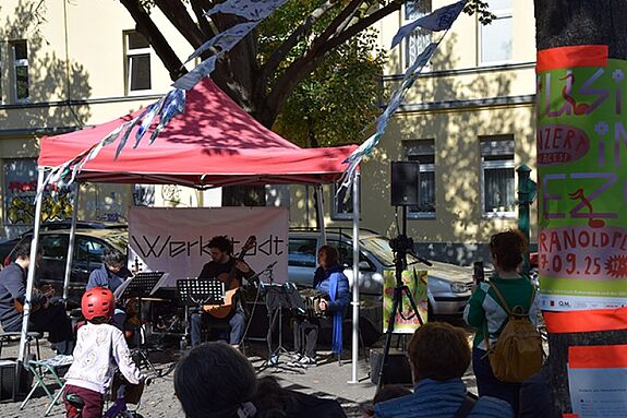 Unter einem roten Pavillon treten Musikerinnen und Musiker bei einem Nachbarschaftskonzert auf dem Kranoldplatz auf.