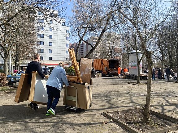 Zwei Personen transportieren Sperrmüll zu einem Sammelplatz. Im Hintergrund steht ein Müllfahrzeug der BSR.