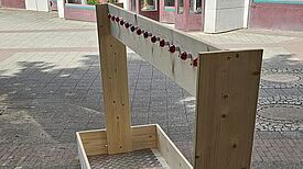 Ein mobiler Kleiderständer aus Holz und mit Rollen steht auf dem Asphalt. 