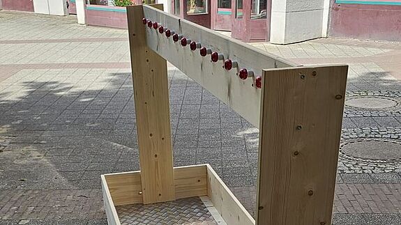 Ein mobiler Kleiderständer aus Holz und mit Rollen steht auf dem Asphalt. 