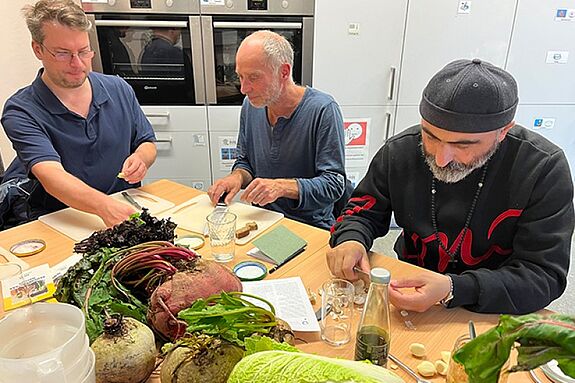 Drei Teilnehmende schneiden am Küchentisch das Gemüse für die Fermentation.