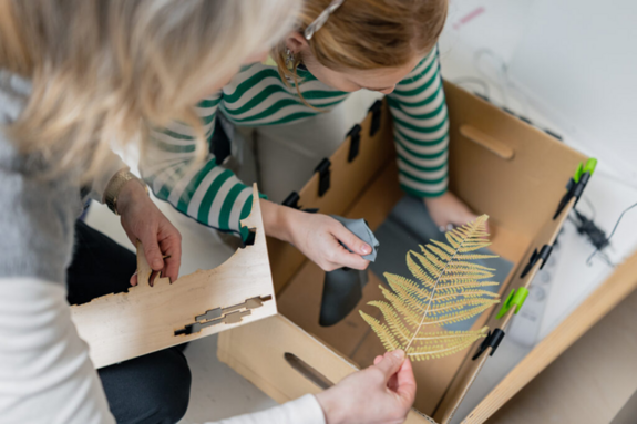 Zwei Teilnehmende legen einen Farn in einen Karton, um ihn im Anschluss zu belichten.  
