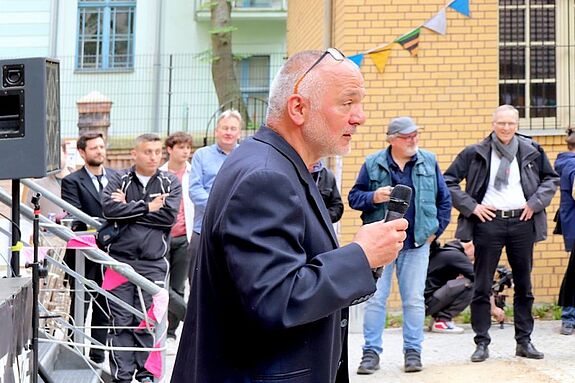 Projektleiter Kemal Özbasi begrüßt die Gäste mit einem Mikrofon bei der Eröffnung der NaunynRitze.