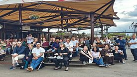 Viele Engagierte sitzen und stehen auf dem Parkdeck des Klunkerkranichs unter einem großen Sonnensegel und nehmen am Sommerfest teil. 