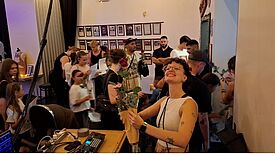Frau mit Blumenstrauß im Vordergrund und zahlreiche Menschen im Hintergrund im Backstage-Bereich der Modenschau im Kulturzentrum Staaken.