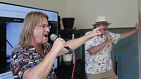 Zwei Männer singen mit Mikrofonen in einem Raum und strecken ihre Arme nach vorn.