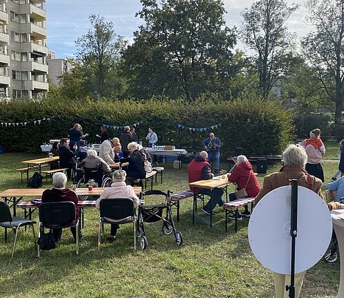 Anwohnende sitzen an Biertischen im Grünen und feiern die Wiedereröffnung des Rosengartens.