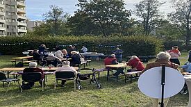 Anwohnende sitzen an Biertischen im Grünen und feiern die Wiedereröffnung des Rosengartens.