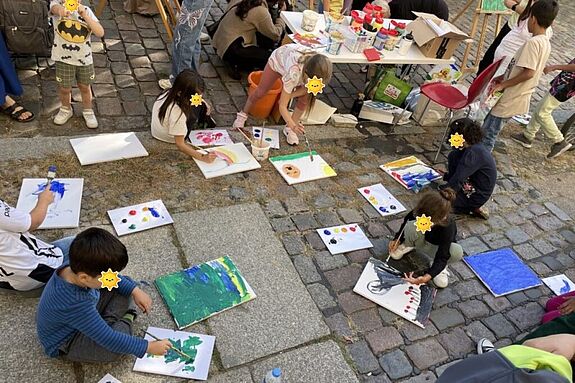 Kinder malen kreativ auf der temporären Spielstraße und nutzen bereitgestellte Farben und Pinsel.