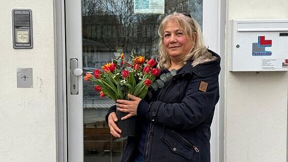 Sidika Öztürk, die ehrenamtlich den Frauentreff organisiert, steht vor einer Tür und hält Blumen.