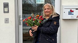 Sidika Öztürk, die ehrenamtlich den Frauentreff organisiert, steht vor einer Tür und hält Blumen.