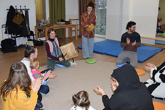 Eltern und Kinder sitzen im Kreis und musizieren gemeinsam. 