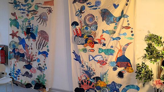 Zwei große Wandbilder aus Stoff zeigen eine bunte Unterwasserwelt mit Fischen. 