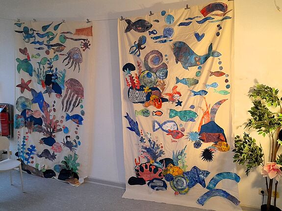 Zwei große Wandbilder aus Stoff zeigen eine bunte Unterwasserwelt mit Fischen. 
