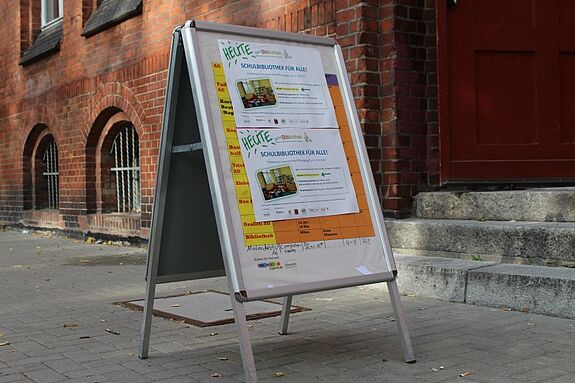 Ein Aufsteller vor der Eduard-Mörike-Schule informiert über die Veranstaltung „Schulbibliothek für alle“ im QM-Gebiet Harzer Straße.