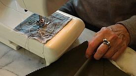 Eine Person sitzt an einer Nähmaschine und näht an einem Stück Stoff. 