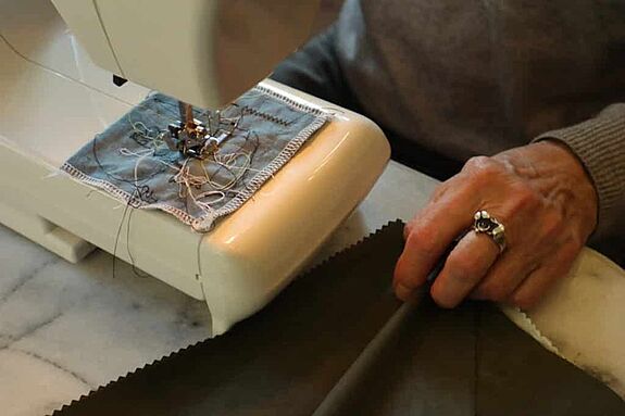 Eine Person sitzt an einer Nähmaschine und näht an einem Stück Stoff. 