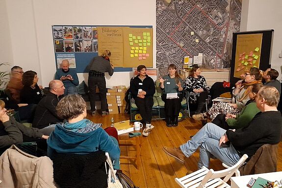 Mitglieder des Quartiersrats sitzen in einem Kreis und diskutieren, während eine Person Notizen auf einem Flipchart anfertigt.