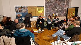 Mitglieder des Quartiersrats sitzen in einem Kreis und diskutieren, während eine Person Notizen auf einem Flipchart anfertigt.