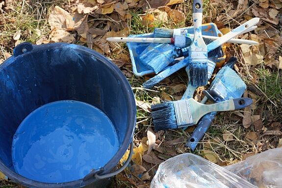 Blaue Farbe und Pinsel liegen auf Herbstlaub.