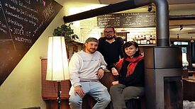 Zwei Engagierte sitzen an der Bar im Kieztreff „Kamine&Wein“, eine weitere Person steht hinter ihnen. 