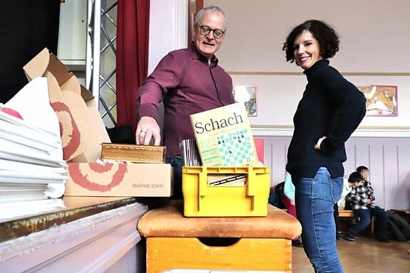 Zwei Personen schauen sich die Ausgaben der Zeitschrift „Schach“ an, die ab sofort im Schachraum der Andersen-Grundschule bereit liegen. 