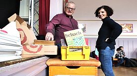 Zwei Personen schauen sich die Ausgaben der Zeitschrift „Schach“ an, die ab sofort im Schachraum der Andersen-Grundschule bereit liegen. 