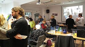 Menschen tauschen sich in einem Veranstaltungsraum beim Neujahrsempfang aus, während im Hintergrund eine Präsentation läuft.