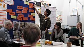 Einige Menschen sitzen an einem Tisch vor einer Präsentationswand. 