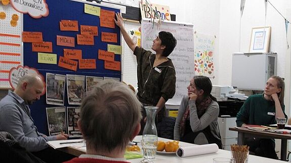 Einige Menschen sitzen an einem Tisch vor einer Präsentationswand. 