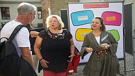 Zwei Frauen und ein Mann diskutieren bei einer Präsentation im Freien während der Bildungswerkstatt im Badstraßenkiez.