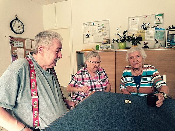 Drei Seniorinnen und Senioren sitzen beim Spielenachmittag an einem Tisch und würfeln. 