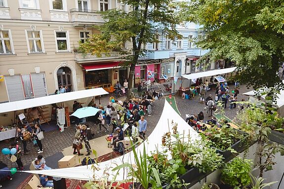 Von oben ist ein Straßenfest im Donaukiez mit Ständen, Besucherinnen und Besuchern und Pflanzen zu sehen.